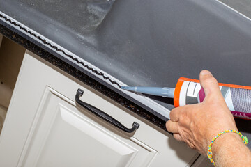 A man applies adhesive sealant to the rim of a countertop kitchen sink. Sink installation