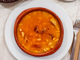 Fabada asturiana served in brown plate with serving pieces