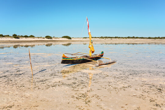 Fisherman piroga (small fishing boat with sail) waiting at the low tide coast on sunny day