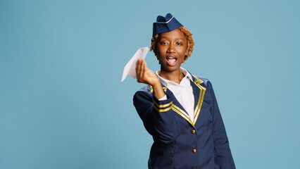 Female model showing folded airplane in studio, playing with paper plane dressed as stewardess....