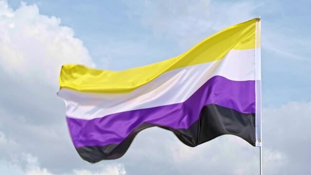 non binary flag waving in the wind in slow motion with cloudy sky in the background