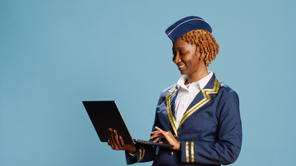 Young air hostess using laptop on camera, navigating online website page and social media app. Professional airliner working in flying industry and holding portable computer, browsing site.