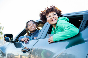 Two young, handsome girls with dark skin are leaning out of a car window as they look up. Concept of travel, vacation. Buy a new car, get the license.