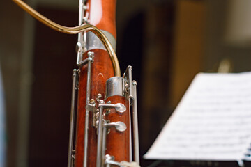 part of the body of a bassoon in the foreground with blurred sheet music in the background
