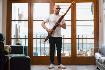 young latin man venezuelan musician in his living room standing playing the bassoon - obrazy, fototapety, plakaty