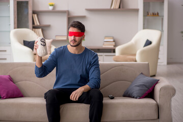 Young blindfolded man holding moneybag at home