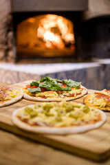 small individual pizzas ready to be introduced into the clay oven with its fire inside
