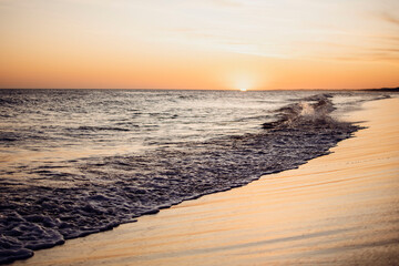 Sunset in the sea with the waves on the shore breaking on the sand in the summer vacation

