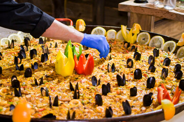 Chef working in the restaurant kitchen preparing a large seafood paella with vegetables, fruits and mussels
