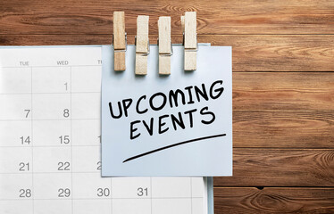Blue sticker attached to a calendar on a wooden background with text UPCOMING EVENTS