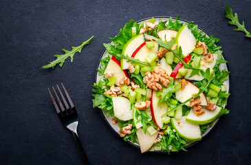 Waldorf salad with red and green apple, celery, lettuce, arugula and walnuts on plate, black table background, top view