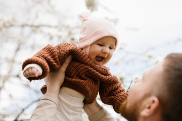 A father lifts up his daughter up in the air while they have fun together in the garden. 