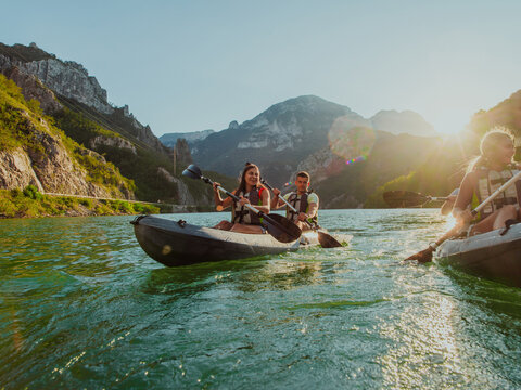 A group of friends enjoying fun and kayaking exploring the calm river, surrounding forest and large natural river canyons during an idyllic sunset.