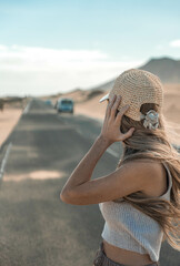 Rear view portrait of blonde woman looking the car on a road in dunes desert