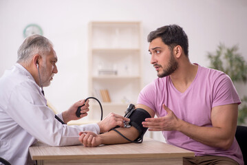 Old male doctor measuring young patient's blood pressure