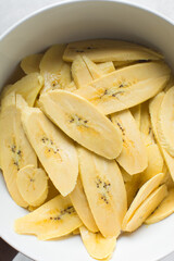 Top view of slices of ripe plantains in a white bowl, slices of yellow plantains for frying, process for making fried plantain