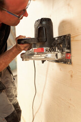 The carpenter is sanding a wooden surface that he holds vertical