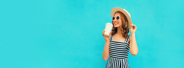 Portrait of happy smiling young woman drinking fresh juice or coffee wearing summer straw hat, dress on blue background