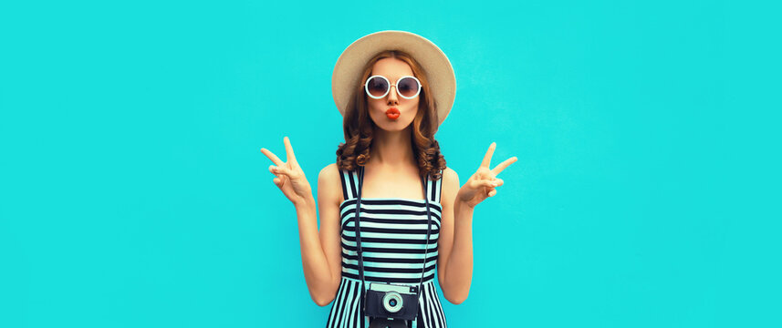 Summer portrait of happy smiling young woman photographer with film camera wearing straw hat, dress, sunglasses on blue background