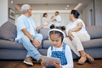 Cute little mixed race girl in casual clothes and headphones using a tablet and listening to music or watching videos at home. Child wearing headphones to block out arguing parents in background