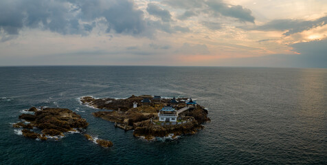 Panoramic view of small Japanese shrine on rocky island in ocean at sunrise