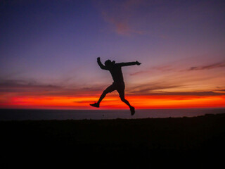 The thrill of adventure with the silhouette of a man jumping near a cliff in front of the ocean at sunset
