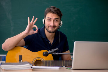 Young male music teacher sitting in the classroom