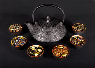 Cast-iron tea kettle surrounded by cups filled with different kinds of loose leaf tea. Tea ceremony.