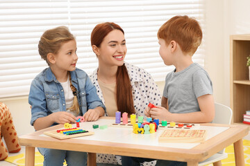 Fototapeta premium Happy mother and children playing with different math game kits at desk in room. Study mathematics with pleasure