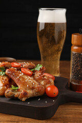 Fototapeta na wymiar Glass of beer and delicious baked chicken wings with ingredients on wooden table