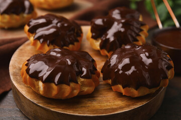 Delicious profiteroles with chocolate spread on wooden board, closeup