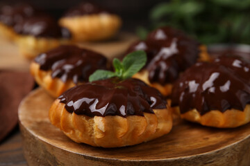 Obraz na płótnie Canvas Delicious profiteroles with chocolate spread and mint on wooden board, closeup
