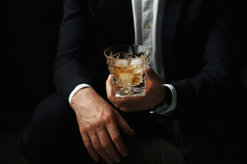 Man holding glass of whiskey with ice cubes on black background, closeup