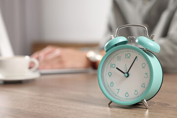 Turquoise alarm clock and man working at table in office, closeup with space for text. Deadline...