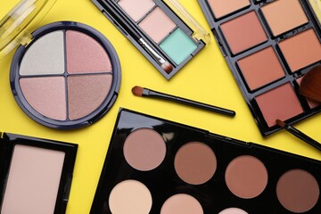 Different contouring palettes and brushes on yellow background, flat lay. Professional cosmetic product