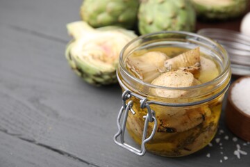 Jar of delicious artichokes pickled in olive oil on grey wooden table, closeup. Space for text