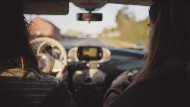 Couple driving in a car at sunset. Young Man and woman friends travel, enjoy road trip, talking, having fun at sunrise, morning or evening road with lens flare. POV from a passenger back seat.