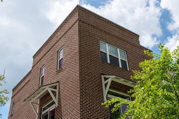 The exterior of a tall brown colored brick building with multiple double hung windows with white trim. The vintage apartment building has a canopy over the lower floor windows to shade the interior. 