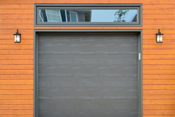 A modern dark brown metal exterior garage door with a small horizontal glass window. The modern...