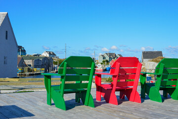 Red and green wooden chairs on a wharf in historic Lunenburg, Nova Scotia. The harbour is...