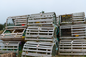 A stack of lobster pots sits on a local wharf out of water waiting for the lobster fishing season to start. The traps are filled with weights and licenses. Some are square and some are round shapes. 