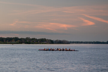 Two teams rowing in shells with multiple teammates at a university competition. The boats are...