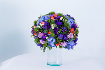 Many kinds of flowers placed in a brightly colored vase in a white setting
