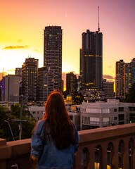 Fototapeta na wymiar beautiful woman in a hat watching the sunset over brisbane city from kangaroo point, city reach boardwalk with amazing view of large skyscrapers by brisbane river, australia, queensland