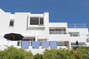 Blue and white striped towels hang over rail outside white stucco Mediterranean style building from road below