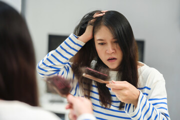 stressed woman suffering hair loss problem with hairbrush in mirror at home