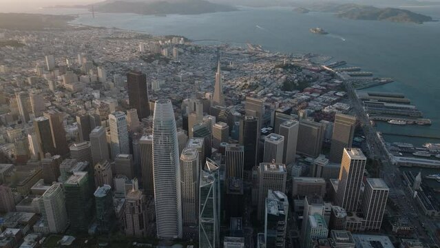 Aerial view of downtown skyscrapers at sunset. Tilt up reveal of sea bay with islands and hilly landscape in distance.