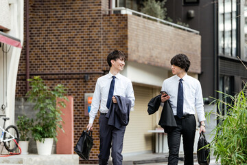 町並みをシャツ姿でスマートフォンを持ち会話しながら並んで歩く2人のビジネスマンの笑顔の男性