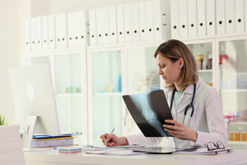 Focused doctor examines x-ray of patient joint making notes