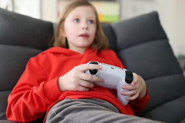 Focused schoolgirl plays video game sitting in armchair